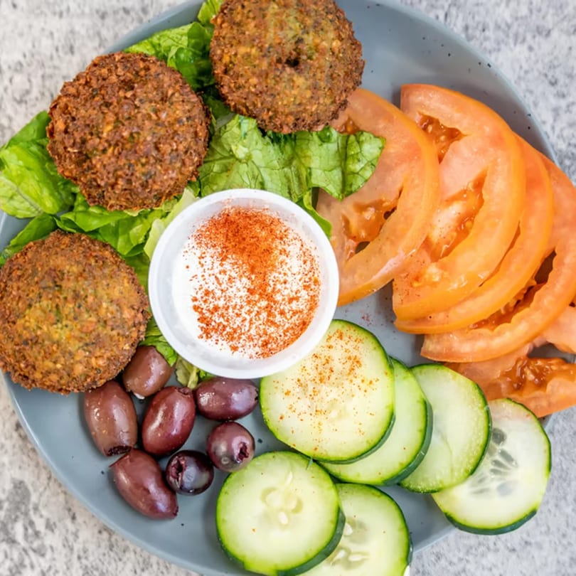 Albasha Express falafel plate with lettuce, tomatoes, cucumbers, olives, and a white sauce.