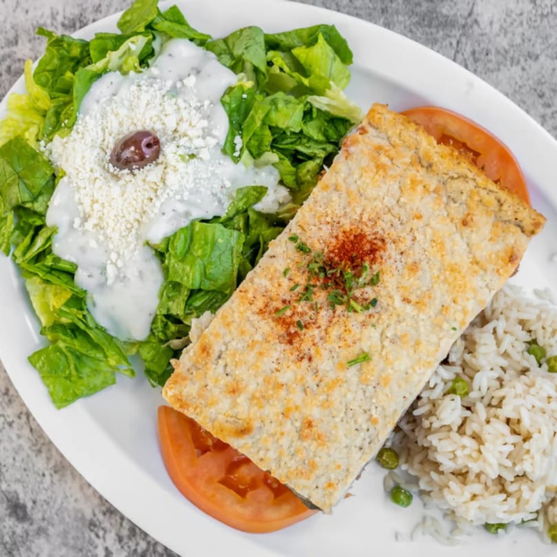 A middle-eastern meal with a baked dish, rice and peas, and a side salad with feta and olive.