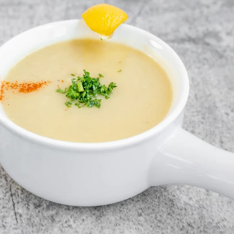 Creamy middle-eastern soup in a white bowl, garnished with parsley, paprika, and a lemon wedge.