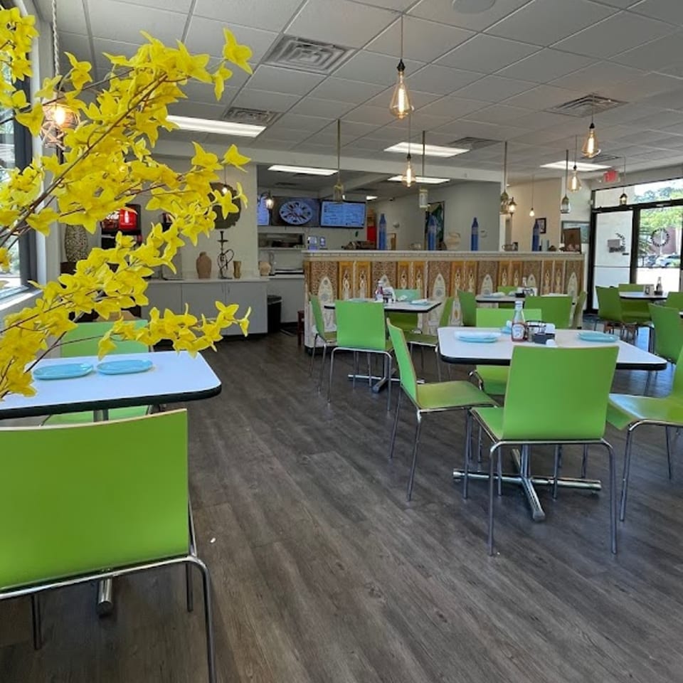 Brightly lit Albasha Express dining room with green chairs, white tables, and a decorative yellow plant.