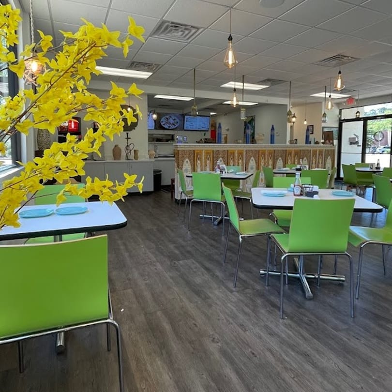 Brightly lit Albasha Express dining room with green chairs, white tables, and a decorative yellow plant.
