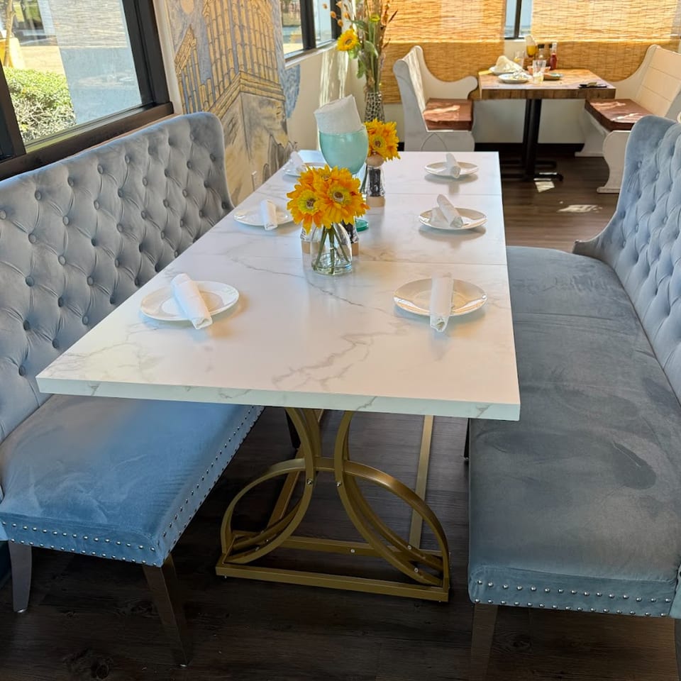Albasha Express dining area with light blue tufted benches, marble table, and yellow flower centerpieces.